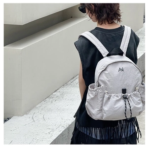 Detail of grey nylon backpack showing the black embroidered AN logo and drawstring front pocket