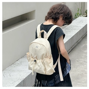 Detail of a beige mini children's backpack with drawstring pocket and AN embroidery detail