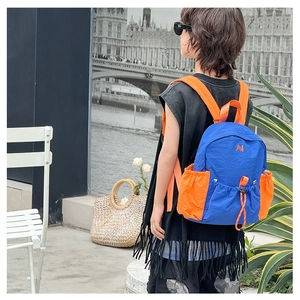 Detail view of child wearing contrast blue and orange backpack with adjustable side drawstring