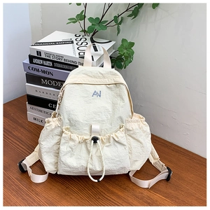 Detail view of cream nylon backpack featuring blue AN logo and drawstring front pocket