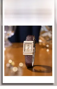 Close-up of square gold watch face with brown pebble texture strap on wood background