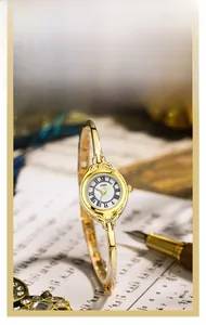 Detail of vintage gold bangle watch with Roman numerals on white dial and slim metal strap