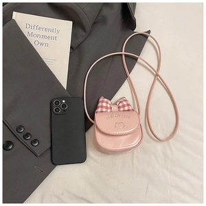 Mini pink shoulder bag with cat embroidery and plaid bow next to a smartphone