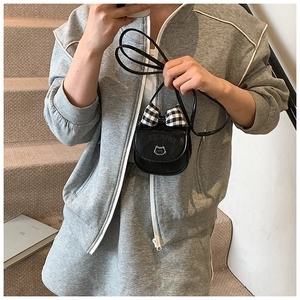 Mini cat-themed crossbody bag with checkered bow detail worn by model on stairs