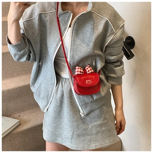 Red cat-themed mini crossbody bag with a plaid bow accent on a grey sporty outfit