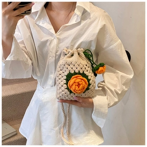 Detail der handgehäkelten Kordeltasche mit orangefarbenen gestrickten Blumenakzenten
