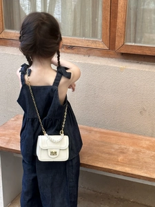 Close-up of a mini white pearl handle bag with gold chain on a denim outfit for girls