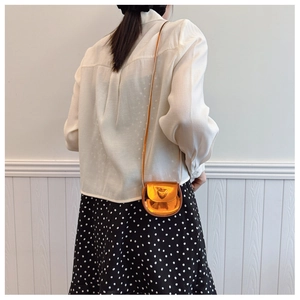 Detailed view of glossy orange mini crossbody bag with heart motif on a shoulder strap