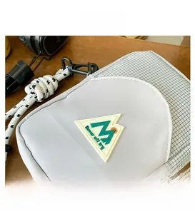 Détail du sac bandoulière en nylon avec motif à carreaux noir et blanc et écusson montagne