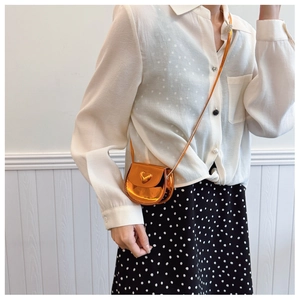 Close-up of a glossy orange heart-shaped mini crossbody bag worn by a child model