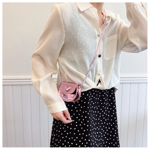 Detail of pink metallic mini crossbody bag with heart buckle on a polka dot dress