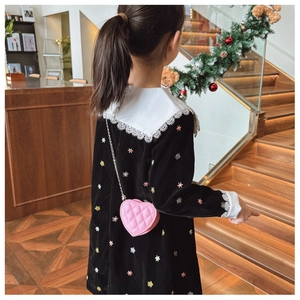 Détail d'un sac cœur matelassé rose avec chaîne porté sur une robe en velours