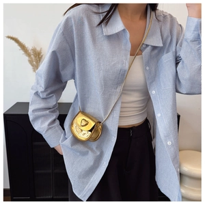 Close-up of golden metallic mini heart crossbody bag with delicate chain strap on model