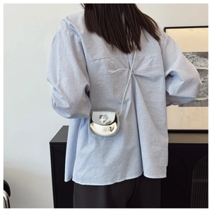 Silver mini heart crossbody bag with glossy finish shown on model in a modern room