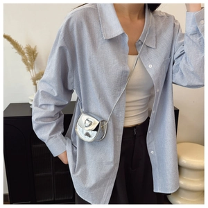 Close-up of a silver mirror heart-shaped mini crossbody bag worn with a striped shirt
