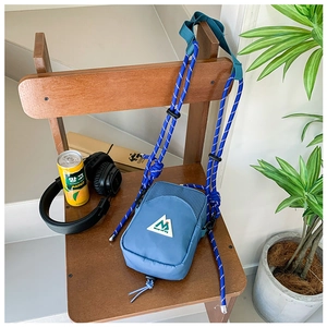 Détail du mini sac bandoulière en nylon bleu avec sangle corde rayée et logo montagne sur chaise