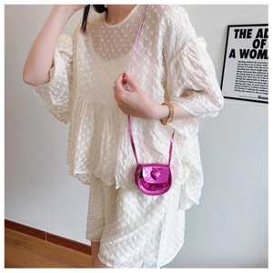 Close-up of heart-shaped mini metallic pink bag paired with white lace outfit for girls