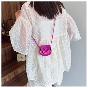 Detail view of mini fuchsia heart-shaped crossbody bag worn by a child in a home setting