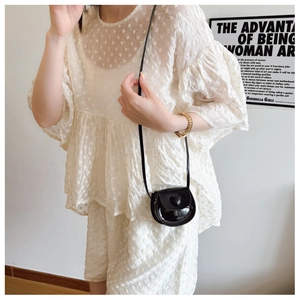 Detail of a shiny black heart-shaped mini crossbody bag worn with a white lace outfit
