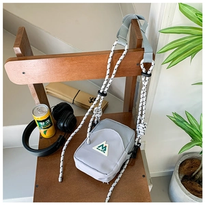 Détail du mini sac bandoulière gris avec sangle en corde tissée et écusson de montagne