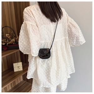 Detail of a black heart-shaped mini chain bag paired with a textured cream-colored outfit