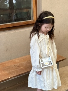 Détail d'un mini sac transparent avec nœud blanc et chaîne dorée sur robe en dentelle
