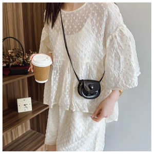 Detail of a mini black heart-shaped crossbody bag on a textured white floral dress