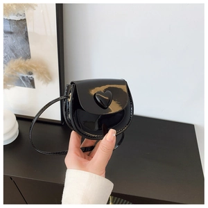 Detail of a black patent leather mini shoulder bag featuring a 3D heart-shaped ornament