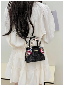 Detail of black faux leather handbag with silk scarf wrap on handle and stone texture