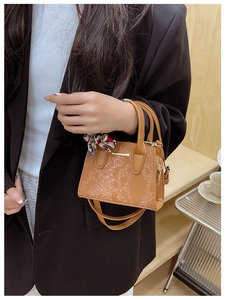 Close-up of model carrying a tan faux snake skin mini bag with decorative silk scarf