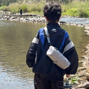 Sac bandoulière tendance pour enfants et coupe-vent tricolore sur rive de rivière