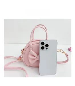 Détail du mini sac rose avec nœud à côté d'un smartphone pour comparer la taille