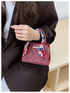 Detail of burgundy snakeskin texture mini bag with silk scarf handle and gold metal bar