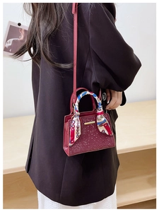 Detail of burgundy stone embossed mini handbag with silk scarf handle and gold bar accent