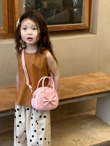 Détail d'un sac rose pour enfant avec grand nœud et accessoires en métal doré