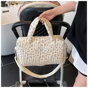 Quilted floral diaper bag hanging on a stroller with adjustable shoulder strap detail