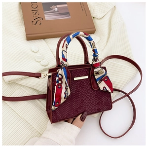 Detail of burgundy stone-patterned mini bag with scarf-wrapped handle and golden bar