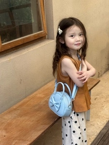 Sac bandoulière rond bleu clair pour enfant avec nœud, porté par une fillette