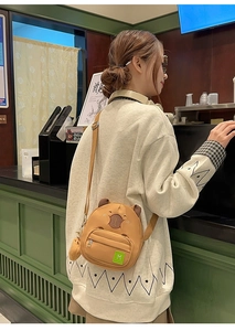Détail d'un sac bandoulière Capybara en toile avec écusson vert et pendentif boule en peluche