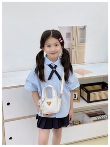 Dettaglio della mini borsa bianca con nappina di perle e logo a triangolo dorato per bimba