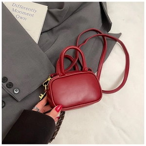 Détail du mini sac bandoulière rouge avec breloque clé dorée sur fond de costume gris