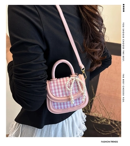 Detail of a pink plaid handbag with pearl bow charm worn as a crossbody bag