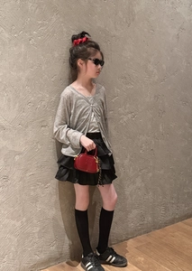 Détail d'un ensemble mode fille avec gilet gris, jupe à volants et petit sac rouge