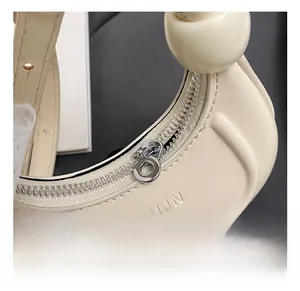 Vue macro d'un sac demi-lune crème avec logo UJN gaufré et poignée en perles élégantes