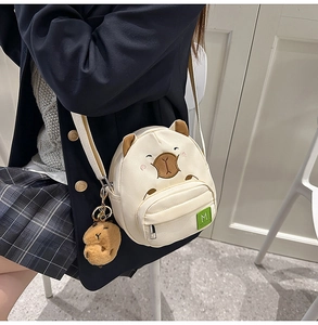 Gros plan du sac bandoulière Capybara crème avec écusson M et porte-clé en peluche
