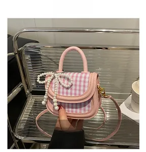 Detail of pink plaid handbag with pearl bow charm on a modern chair display