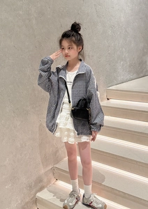 Détail d'un mini sac noir porté avec une veste à carreaux et une jupe en dentelle blanche