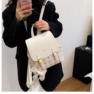 Detail of trendy small backpack featuring cream flap and teddy bear pendant accessory