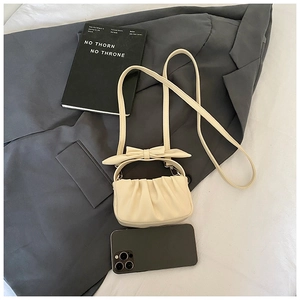 Mini beige ruffled bag with bow detail shown next to a smartphone for size reference