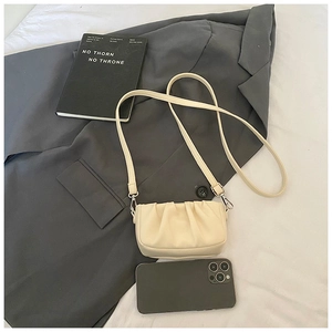 Détail d'un sac nuage plissé blanc crème avec bandoulière en cuir sur une veste grise